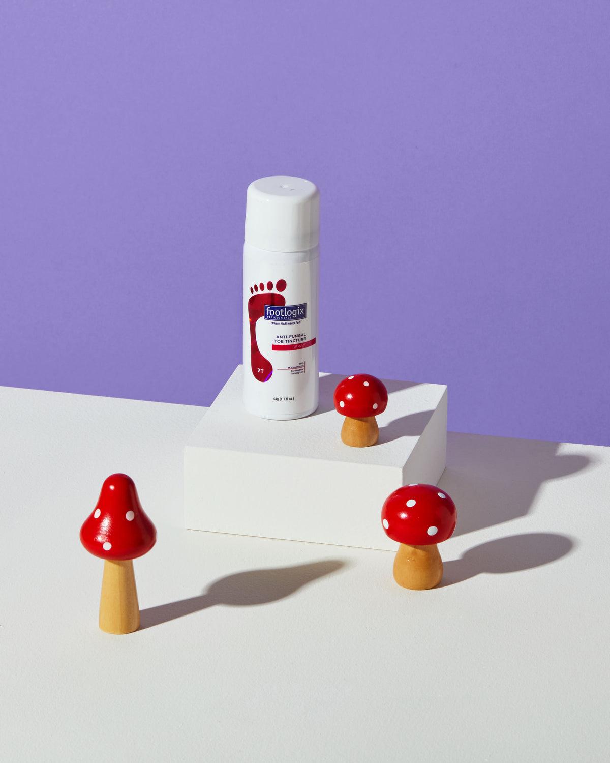 Footlogix Anti-Fungal Toe Tincture bottle with small red decorative mushrooms on a white pedestal